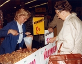Två kvinnliga kunder står på var sin sida om en papp-disk där det ligger flertalet upplagda wienerbröd. På papp-disken står det textat 