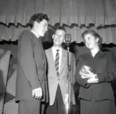 Tre personer på en scen vid en mikrofon.