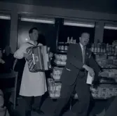 En man i vit rock som spelar dragspel och en man i kostym som gör något framträdande.