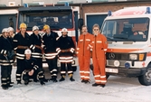 Mölndals brandstation i Trädgården, Mölndal, på 1980-talet. En samling brandmän och ambulansförare står uppställda vid sina fordon.