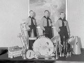 Foto av okänd orkester, en kvartett, fotograferad på Varbergs Hotell. Pianisten saknas här men ses på övriga bilder, GB2_3191-3193. Musikerna är klädda enhetligt och på bastrumman finns karikatyrer av männen tecknade. Framför dem står instrumenten uppställda: dragspel, saxofoner, trumpeter, gitarr, fiol och klarinetter. Denna bild har använts för att kopieras in på flygeln i bild GB2_3192 med pianisten.
(Se även bildnr GB2_3192-3194)