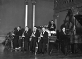 Okänd orkester med sex män spelar på Stadshotellet i Varberg. På bilden spelas saxofon, trummor och flygel, men även dragspel, ståbas, gitarr, trumpet och fioler kan bandet traktera.