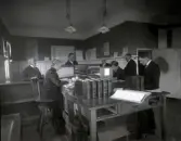 Interiör av mindre handelsbankskontor, möjligen i Åseda. Damen i mitten är troligen huvudbokhållare till vilken de andra hade att redovisa.