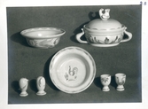 Servis från Bo Fajans, tidigt 1900-tal. En skål, äggkarott med lock, salt- och pepparkar, ett fat samt två äggkoppar, alla dekorerade med tuppar.