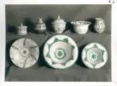 Tre mindre skålar två med lock, två mindre vaser samt tre fat i olika storlekar från Bo Fajans, tidigt 1900-tal. På fotot har dekoren på två fat delvis ritats i med grön penna.