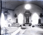Interiören av en kyrka. Till vänster ser man predikstolen med baldakin. I mitten ser man altaret med altartavla och altarbord med altarskrank framför. Några kristallkronor finns också med.
