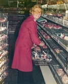 Berit Thörnqvist, klädd i röd rock, packar upp bröd i brödavdelningen, Domus Mölndals C efter 1976.