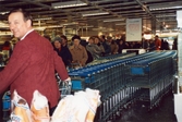 K-marknads invigning på Frölundagatan (nu: Brogatan) cirka 1985 - 1986. En lång kö med kunder ringlar in i butiken. En manlig expedit står leende vid kundvagnarna.