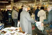 Flertalet kunder med kundvagnar som köar till kassorna för att betala, K-marknad efter 1985/86. På vägen fram till kassorna finns olika erbjuden utplacerade.