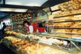 Två kvinnliga expediter klädda i röda rockar står innanför bröddisken, Brödavdelningen på K-marknad, Mölndals C efter 1985/86. Hyllorna är fyllda av allehanda bakverk.