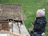 Invigning av Fagereds natur- och kulturstig i Lindome år 2008. Ett litet barn sitter på knä framför en stenåldersby i mini-format (se 1988_0229). Byn består av ett hus, ställningar för att torka hud samt trädjur. 
Fagered bjuder på kommunens bäst bevarade järnåldersmiljö. Här finns rester av en gammal hålväg, spår av äldre jordbruksmark och ett 40-tal gravar. 
Relaterade motiv: 2024_1300 - 1308.