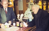 Karl Jansson expedierar Möller vid SJ, på den förres allra sista arbetsdag. Systembolaget, Norra Järnvägsgatan, Växjö.
Färgfoto, ca 1965.