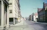 Kungsgatan, Växjö, i korsningen Kungsgatan/Norrgatan. Till vänster skymtar Frimurarhuset och till höger syns den s.k. Sjögrenska skolan m.m.
Färgfoto ca 1965.