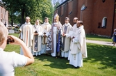 Prästvigning 1974 (?). De nya prästerna har samlats utanför domkyrkan, tillsammans med biskop Sven Lindegård. Till höger om biskopen syns Gunnar Hyltén-Cavallius. 
Färgfoto.