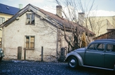 Ett förfallet hus på en innergård någonstans i centrala Växjö. En bil står parkerad vid gaveln.
Färgfoto ca 1970.