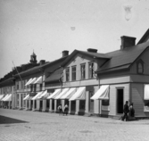 Hörnet av Torggatan och Östra långgatan i Varberg. I bottenvåningen av hörnfastigheten ligger en musik- och pappershandel med bostad på ovanvåningen. Här inrättade fotograf Gustaf Björkström sin fotoateljé och bostad 1906. Ett takfönster togs då upp i det bortre takfallet. Se även bildnr GB2_6738.