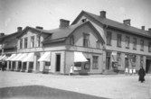 Fotograf Björkströms bostad och fotoateljé på ovanvåningen i hörnet av Torggatan och Östra Långgatan i Varberg. Ingången ses till höger vid Östra Långgatan, granne med ett café, och på gaveln sitter ett skåp med reklam för hans fototjänster. Ateljén låg i bortre änden av huset längs Torggatan. Se även bildnr GB2_6737.