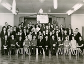 Egnahemsföreningens 20-årsjubileum, okänd plats cirka 1965. Flertalet medlemmar står eller sitter på scenen. Någon håller upp en skylt med texten 