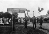 De fyra pojkarna bär symbolerna som ska dekorera midsommarstången, tuppen, klotet, pilen och svenska flaggan. 1910-tal