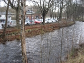 Vy från Pixbovägen åt sydost över Mölndalsfallen samt komplementbyggnader till Grevedämmets skola och dess södra parkering (Pixbovägen 5) med parkerade bilar, Mölndal år 2011. Ett staket sitter utmed forsens stensatta sida. I fonden till höger ses en stor parkering på Pixbovägen 7. Dokumentation inför ombyggnation.
Relaterade motiv: 2024_1365 - 1412.