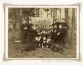 En grupp militärer har slagit sig ner vid ett bord med diverse spritdrycker ute i naturen. På en skärm bakom dem kan man se en skylt med text: 