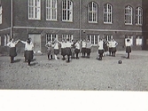 Gymnastik på Rosenfredsskolans/Södra folkskolans gård. Eleverna ser ut att göra någon danslek och på gården ligger en boll. Troligen 1920-talet.