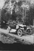 Bil som är tillverkad 1920-1922 med passagerare på skogsväg. Vid ratten sitter Karl Gustavsson i Håfors Idala och bredvid honom sitter Emil Karlsson Hårred (möjligen Herred), Gällinge. I baksätet sitter tre personer.