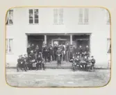 En grupp underofficerare (?) har samlats på trappan till en officersmäss. 1870-tal.
Okänt regemente, okänd ort.