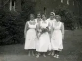 Fem kvinnliga sjukvårdbiträden/undersköterskor står på gräsmattan framför Mölndals sjukhus 1939 - 1941. Kvinnan i mitten håller en bukett blommor i handen. Bilder från fotoalbum, tagna från södra sidan av Länsmansgatan vid Mölndals lasarett/sjukhus 1939 - 1941 på bland annat givarens mor Ester (född Johansson) tillsammans med kollegan/väninnan Aina Englund. De arbetade på den manliga kirurgavdelningen som vårdbiträden/undersköterskor.
Relaterade motiv: 2024_1542 - 1617.