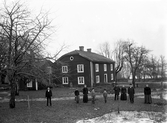 Familj uppställd framför mangårdsbyggnad. Okänd plats, ca. 1905.