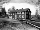 Bostadshus vid grusväg på okänd plats i Kronobergs län. Många människor uppställda framför huset.