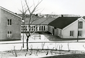 Nya församlingshemmet S:t Jakobsgården i kvarteret Kyrkbacken, Hudiksvall. Bilden visar innergården med utsmyckat staket mot gatan. I förgrunden ett träd och buskar utan löv.