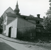 Rivet skjul i kvarteret Kyrkbacken 2, Hudiksvall. Kvar syns huset med nr 1. I bakgrunden syns gaveln och tornet på kyrkan. Till höger i rivningsbråtet anas en cykel på marken.