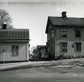Repslagaregatan, kvarteret Kyrkbacken 2, Hudiksvall. Till höger syns en byggnad i två våningar och bortanför det en låg byggnad. Några bilar står parkerade utmed gatan. Till vänster Prästgården. I bakgrunden anas en flaggstång.