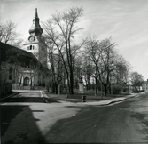 Kyrkan och Olof Bromans byst, Bromansparken, Hudiksvall. Till vänster syns en kyrkportal. Närmast i bild står en parkbänk.