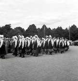 Jubileumsutställningen. Invigningen. 
Ett antal kvinnor i Värendsdräkt tågar in på planen framför
hedersläktaren.