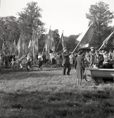 En fanborg tågar in på en äng, vid ett midsommarfirande.