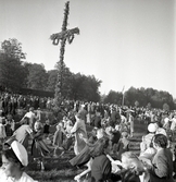 Massor av människor dansar runt en midsommarstång.