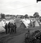 Oxtorget, midsommardagen 1942. Vy över en massa olika tält. I förgrunden syns en mängd cyklar och i bakgrunden syns ett antal bostadshus.