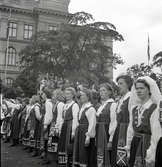 Jubileumsutställning. 
Kvinnor i Värendsdräkt. I bakgrunden syns en del av Växjö
Högre Allmänna Läroverk.