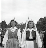 Jubileumsutställning. 
Kvinnor i olika folkdräkter. I bakgrunden skymtar en del av
invigningspubliken.