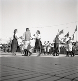 Jubileumsutställning. 
Folkdansuppvisning. Ett folkdanslag i Värendsdräkt m.m. visar upp
sig på en dansbana.