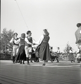 Jubileumsutställning. 
Folkdansuppvisning. Ett folkdanslag i Värendsdräkt m.m. visar upp
sig på en dansbana.