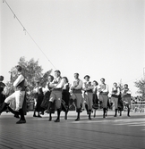 Jubileumsutställning. 
Folkdansuppvisning. Ett folkdanslag i Värendsdräkt m.m. visar upp
sig på en dansbana.