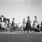 Jubileumsutställning. 
Folkdansuppvisning. Ett folkdanslag i Värendsdräkt m.m. visar upp
sig på en dansbana.