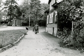 Bebyggelse vid Trädgårdsgatan i Trädgården, Mölndal, år 1988. Två personer och en hund framför huset Trädgårdsgatan 10, även kallat 