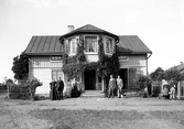 Familj stående framför okänt bostadshus, ca. 1900.