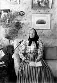 Äldre kvinna i soffa i vardagsrum eller liknande, ca 1900.