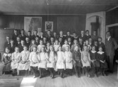 Skolklass i klassrum, uppställda för klassfoto. Ca. 1912, okänd plats, troligen Kronobergs län.