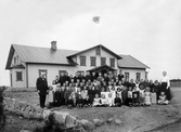 Klassfoto. Troligen två skolklasser med lärare uppställda framför skolan. Ca. 1900. Okänd plats, troligen i Kronobergs län.